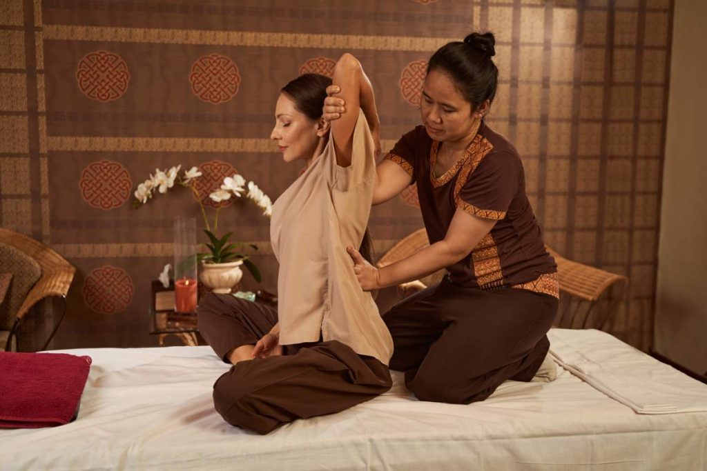 Female sitting on couch with her eyes closed during upper back stretch performed by masseuse